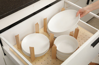 A person's hand is reaching for a white plate from a drawer with wooden dividers, which are neatly arranged inside the drawer.